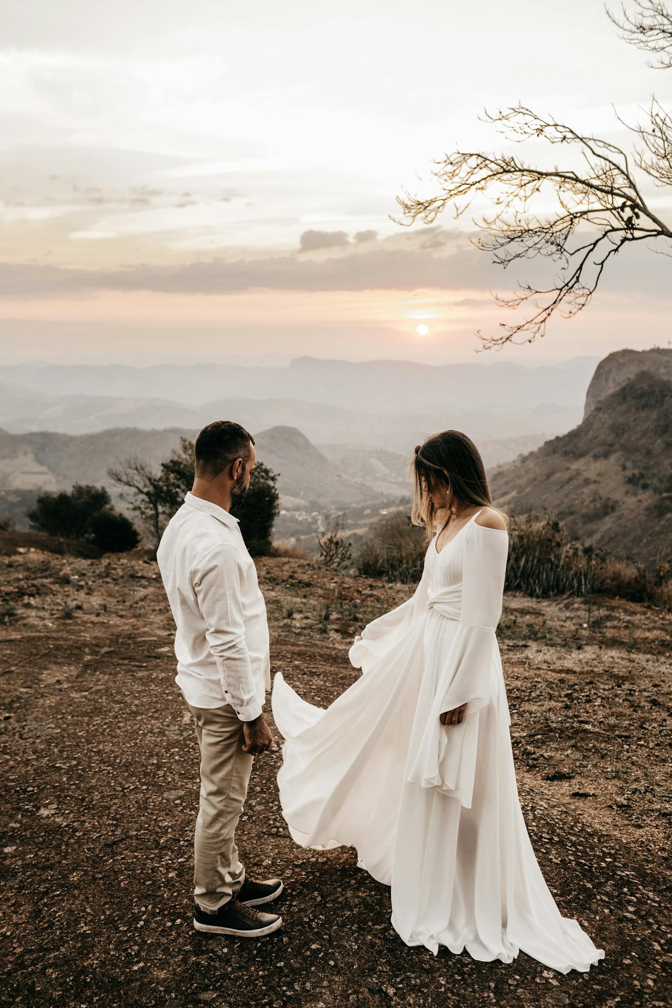 A loving couple in wedding attire share a romantic moment at sunset on a scenic mountain landscape.